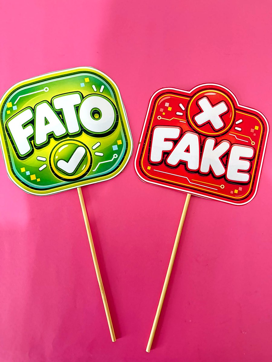 Foto real das plaquinhas FATO, em verde, e FAKE, em vermelho, presas em palitos de madeira sobre fundo rosa
